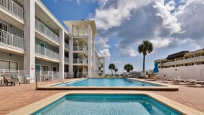 A pool area with a clear blue pool, white balconies, and a brick walkway.
