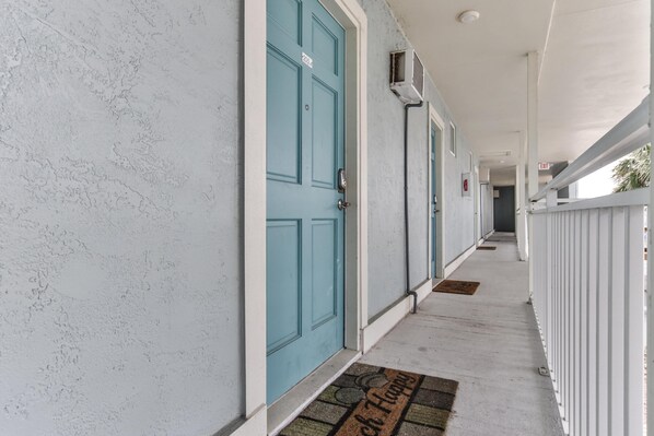 A corridor with teal doors, white walls, and a white railing.