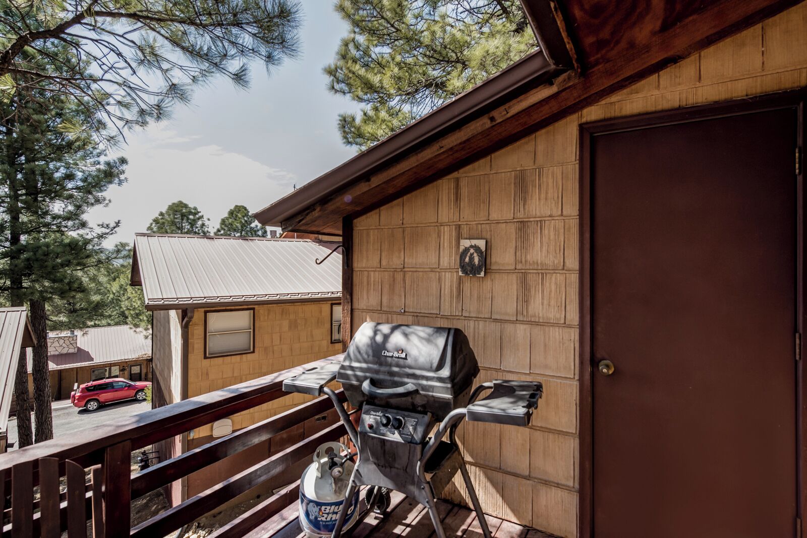 A wooden cabin with a barbecue grill on the balcony, a door, and a small window.