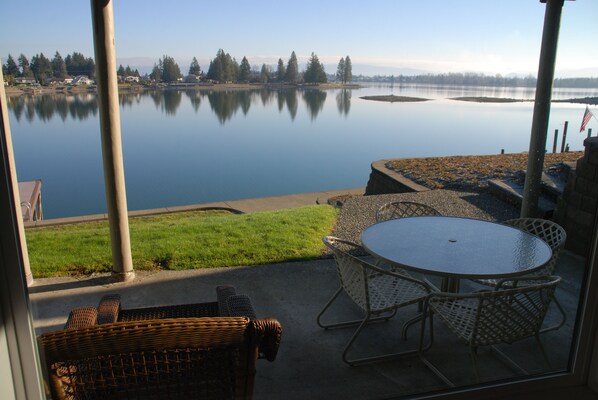 Relax on the patio overlooking a serene lake with a tranquil view of the surrounding trees and sky.