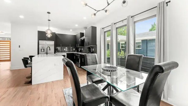 A modern kitchen with dark cabinetry, a central island, and a dining area with a glass table and black chairs. - Top Notch 2 (Atlanta)