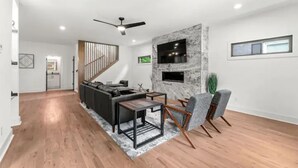A modern living room with a sofa, coffee table, and chairs, a fireplace, and a staircase with a railing. - Top Notch 2 (Atlanta)