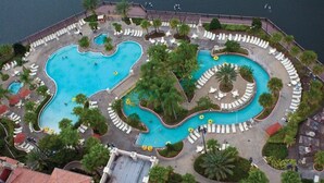 An aerial view of a resort with a large central pool, multiple smaller pools, and sun loungers arranged around the pools.