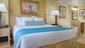 A hotel room with a large bed, two bedside tables, a nightstand, a dresser, and a bathroom with a sink and mirror.