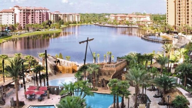 A resort with a large central pool, palm trees, and a bridge connecting different areas.