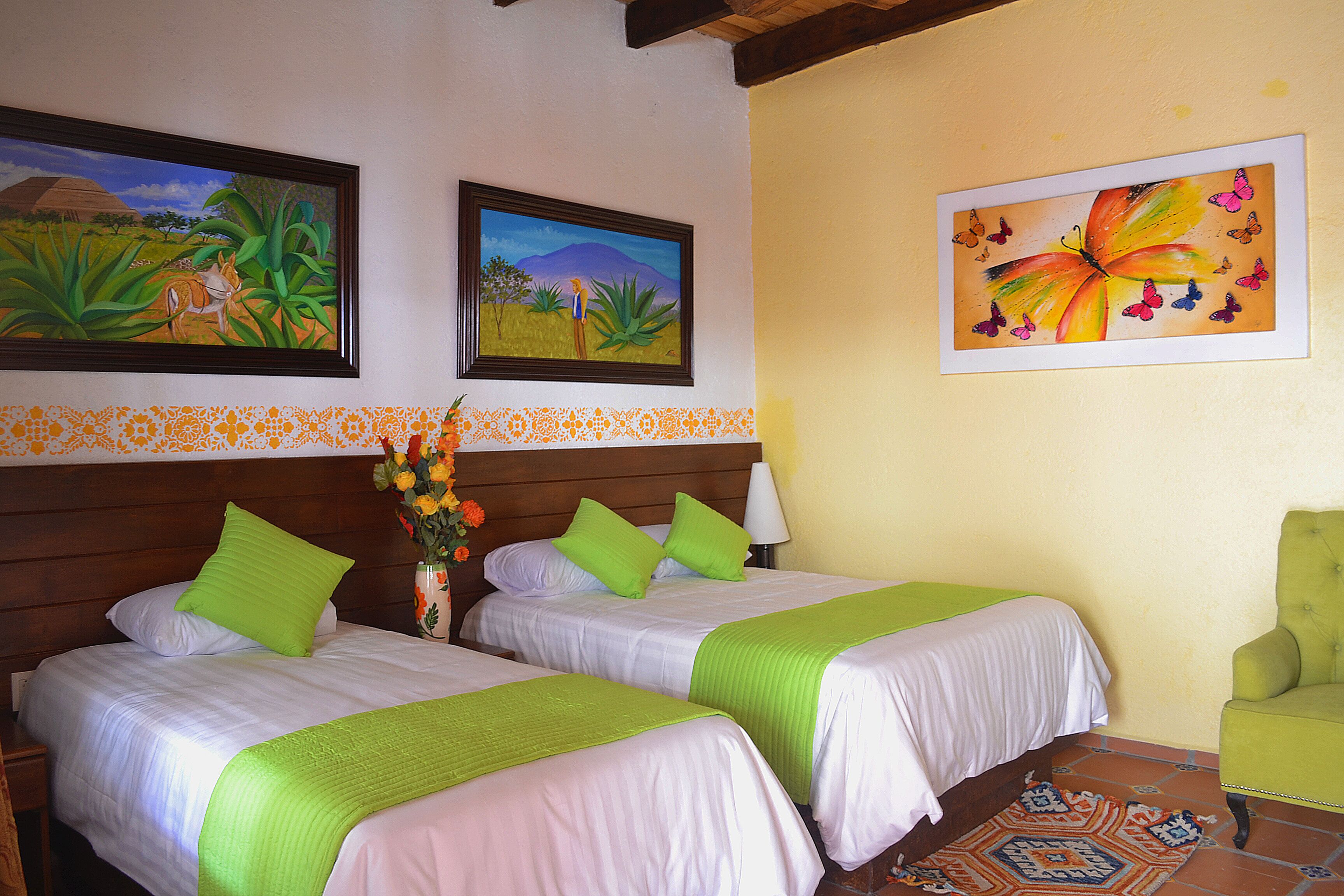 Een hotelkamer met twee bedden, een groene stoel en twee schilderijen aan de muur.