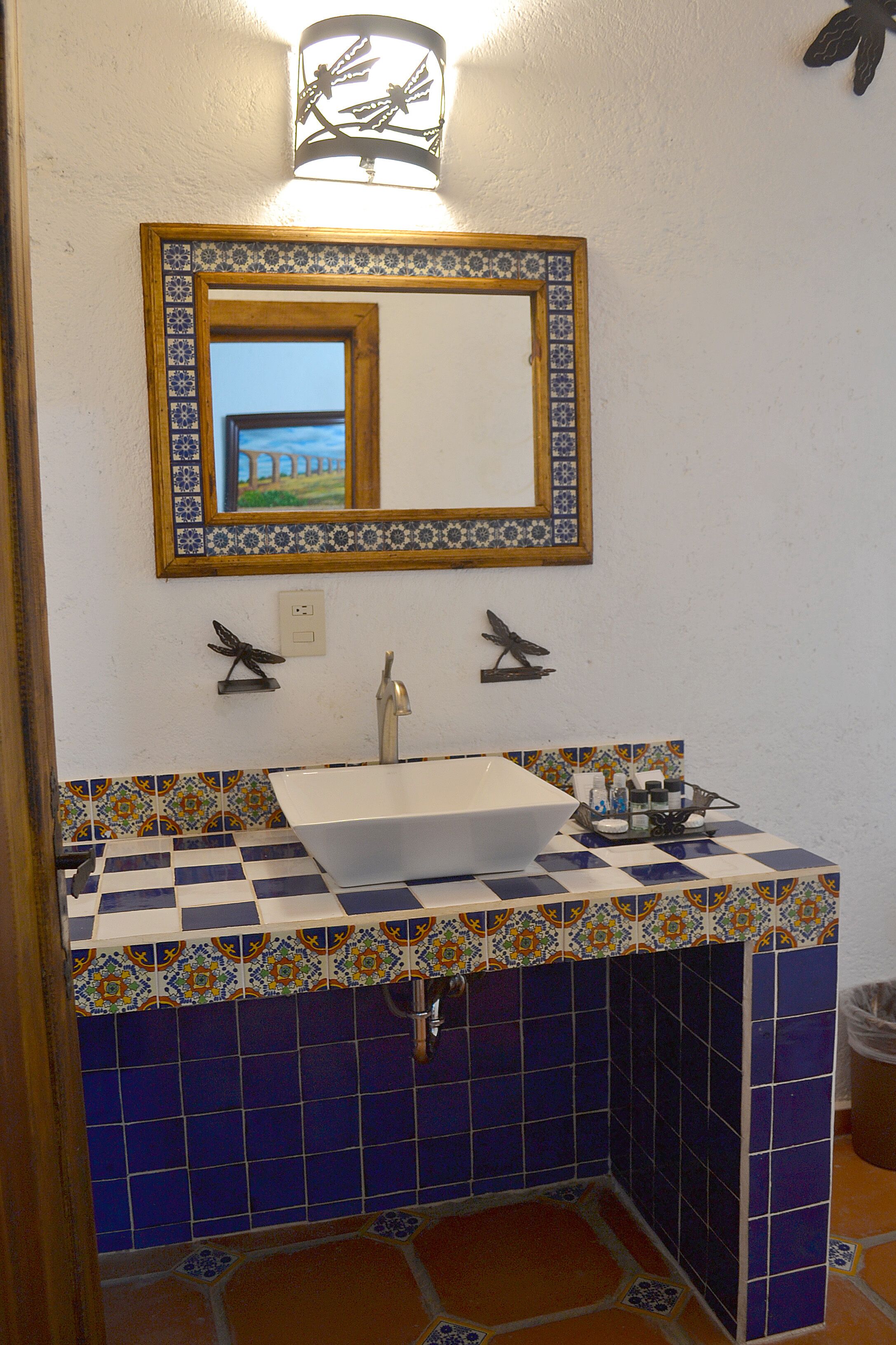 A bathroom with a white sink, blue and orange patterned tiles, a decorative mirror, and a wall-mounted light fixture.