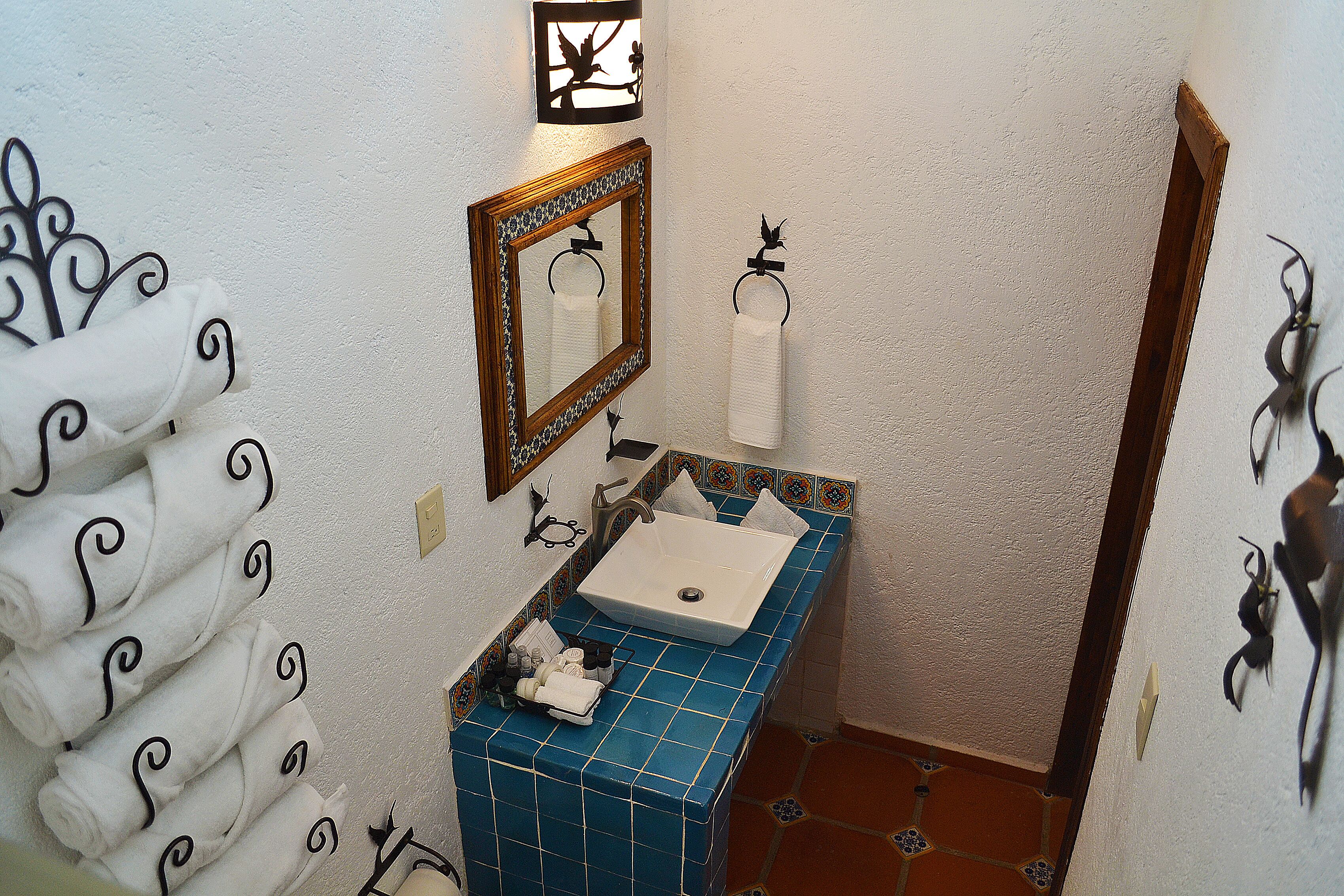 A bathroom with a blue tiled sink, a mirror, and a towel rack with neatly folded towels.