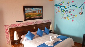 A neatly made bed with blue pillows, a white towel, and a framed picture above it. - La Casona Pirámides (San Martin de las Pirámides)