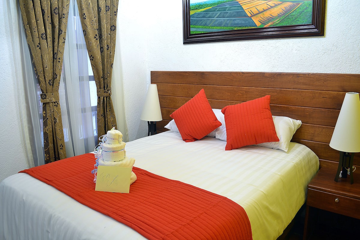 Ein Hotelzimmer mit einem aufgeräumten Bett, einer roten und weißen Bettdecke und einem Zettel auf dem Bett.