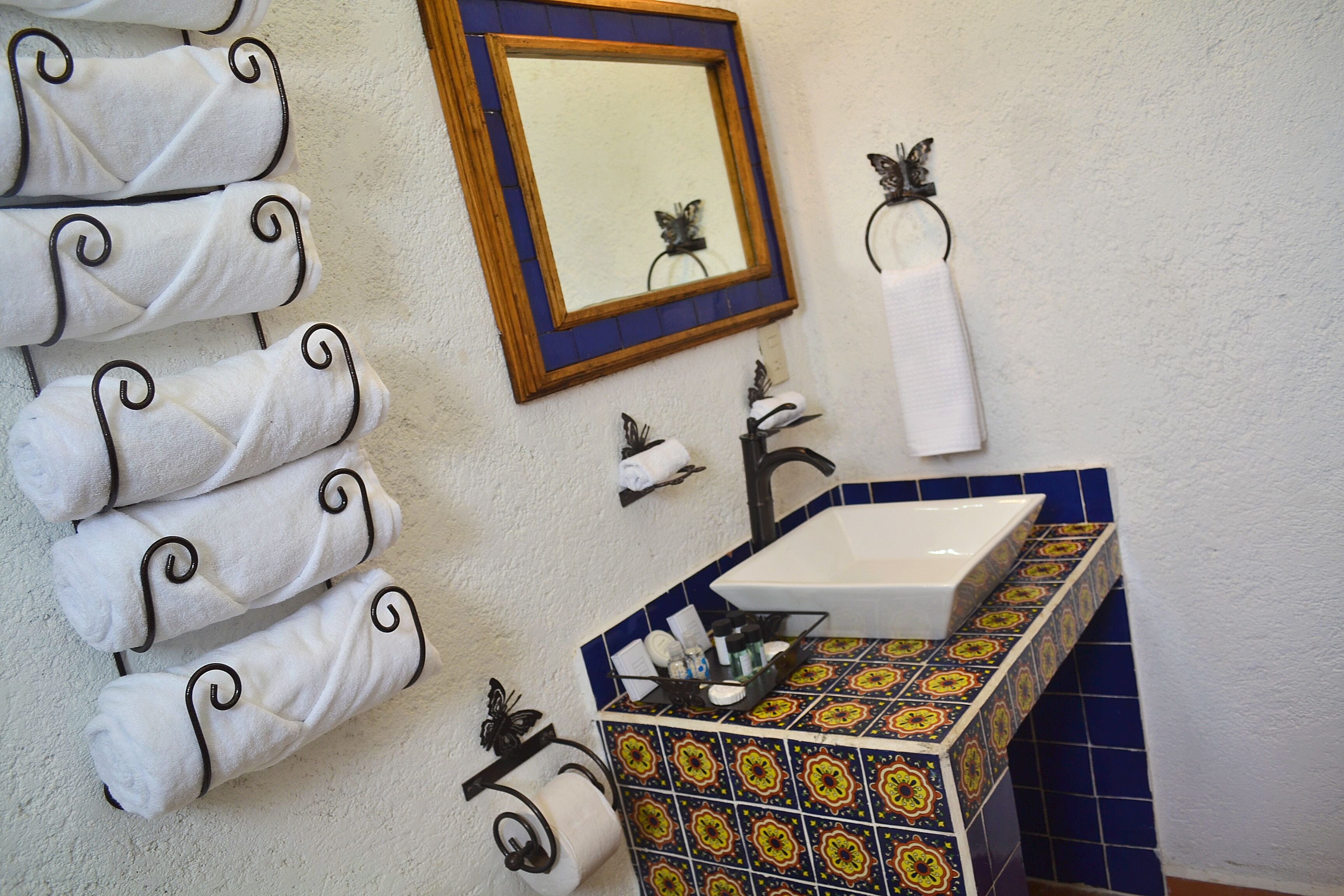 Une salle de bain avec un lavabo carrelé, un miroir et des serviettes soigneusement pliées, rangées sur un porte-serviettes.