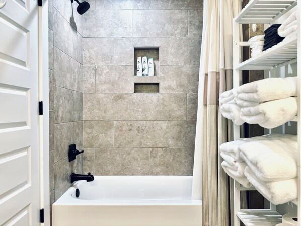 A modern bathroom with a bathtub, a shelf with toiletries, and a towel rack. - Modern 3 bedroom close to the bay and downtown! (Fairhope)