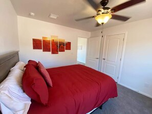 A bedroom with a large bed, a ceiling fan, and a wall with multiple framed pictures.