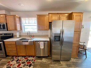 A kitchen with wooden cabinets, stainless steel appliances, a water dispenser, and a patterned rug. - 3BR Family Home | Red Rock Views+Stargazing (Kanab)