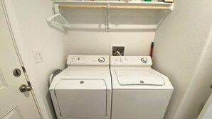 Una lavanderia con due lavatrici e asciugatrici bianche ad accesso frontale, uno scaffale di legno sopra e una porta con pomello.