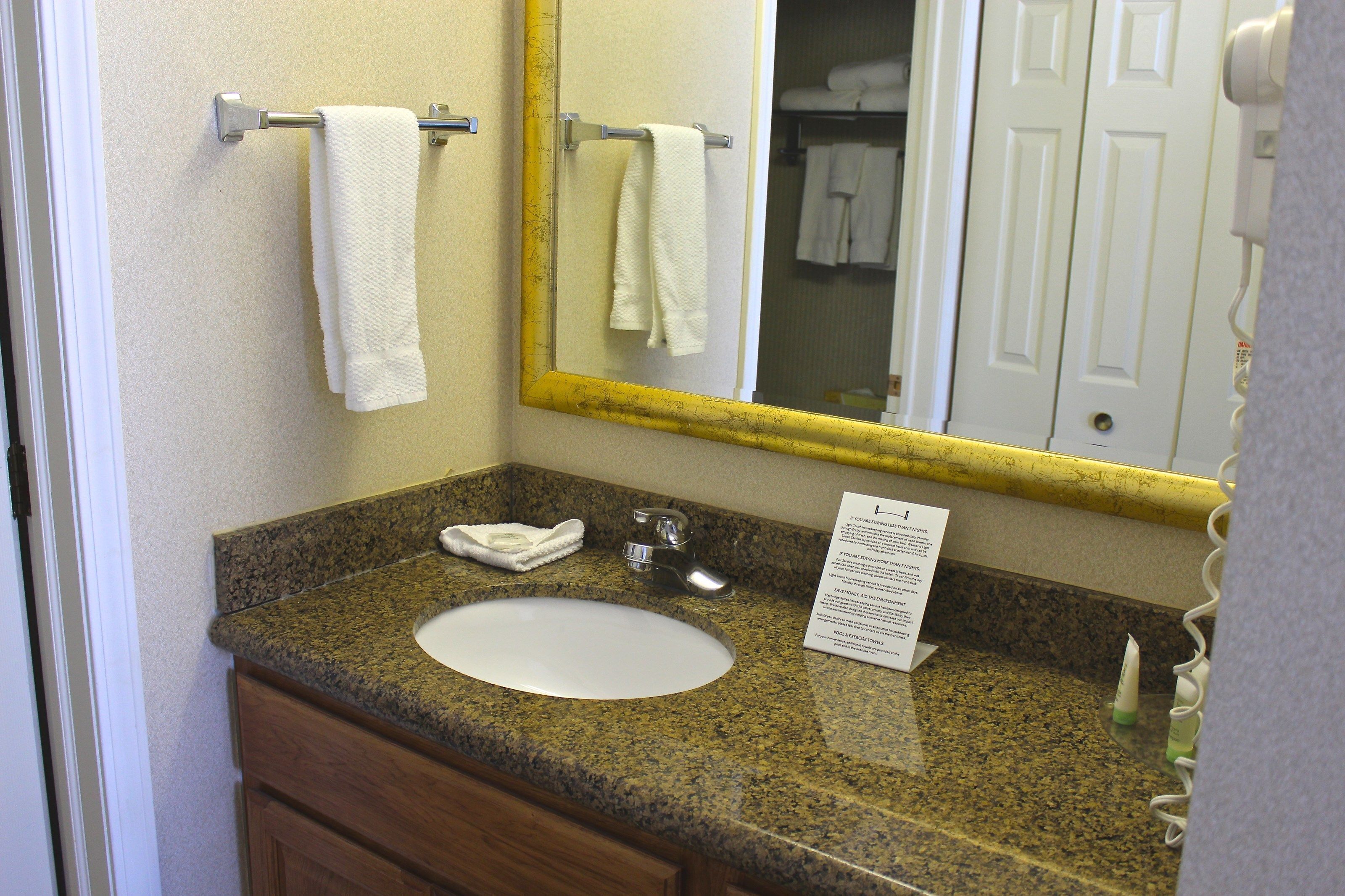 Un bagno con un piano in granito, un lavandino bianco, uno specchio con cornice gialla e un portasciugamani con due asciugamani bianchi.
