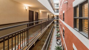 Corredor de hotel com uma passarela central, um edifício vermelho à direita e teto de vidro acima.