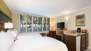 Quarto de hotel com duas camas, uma kitchenette pequena, uma televisão e uma janela com persianas.
