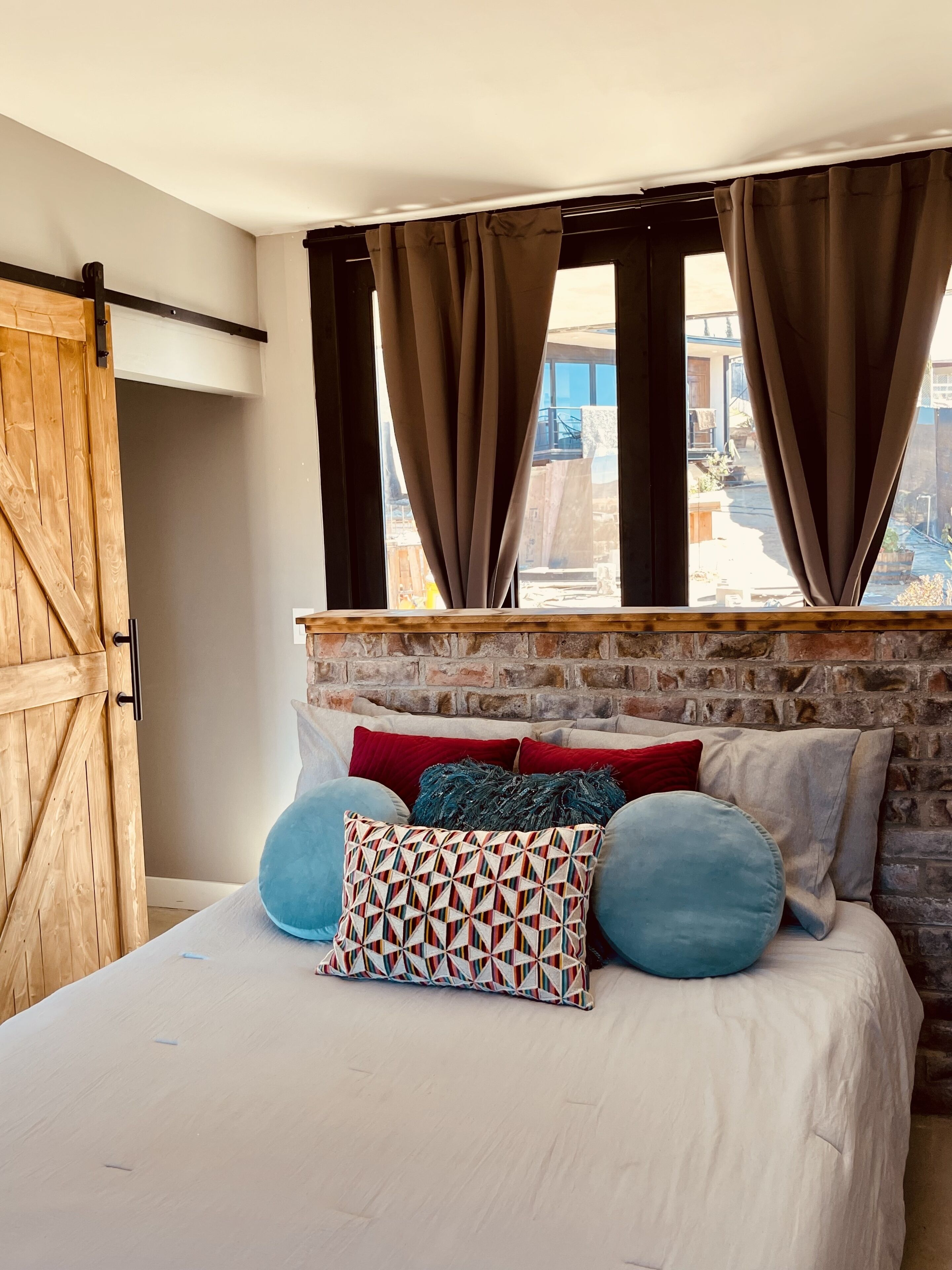 A bedroom with a bed, a wooden door, and a brick wall.
