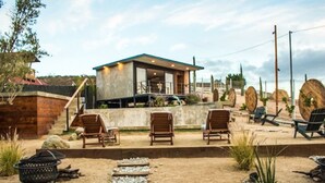 A modern outdoor lounge area with a pool, lounge chairs, and a small building with a glass facade.