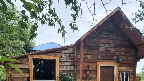 A rustic wooden cabin with a large window, a door, and a small porch area with two red chairs. - The Bunkhouse-within walking distance to Main Street Augusta (Augustaa)