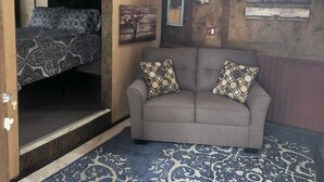 A cozy room with a sofa, patterned cushions, a blue patterned rug, and wooden walls with artwork. - The Bunkhouse-within walking distance to Main Street Augusta (Augustaa)
