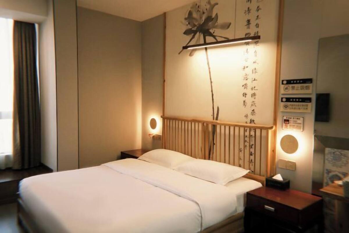 Una habitación de hotel con cama, mesitas de noche, una lámpara de pared y un adorno sobre la cama.
