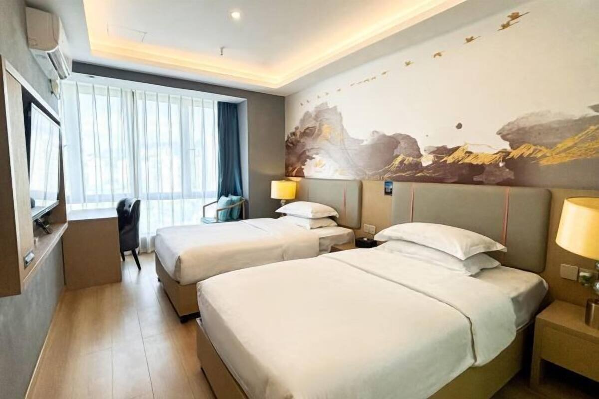 Habitación de hotel con dos camas, un escritorio, una silla y un ventanal con cortinas.