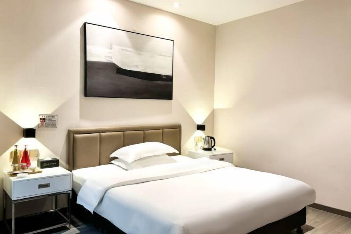 Una habitación de hotel con una cama, mesitas de noche, cafetera y una obra de arte colgada en la pared.