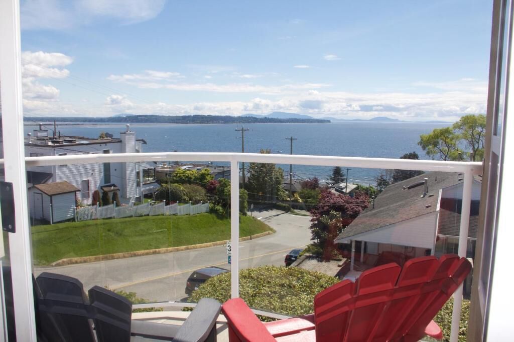Ein Balkon mit roten Stühlen, Blick auf das Meer und eine Wohngegend im Hintergrund.