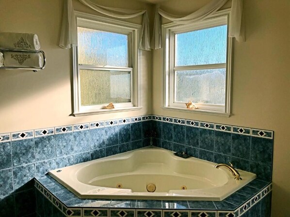 A bathroom with a freestanding bathtub, two windows with curtains, and a towel rack.