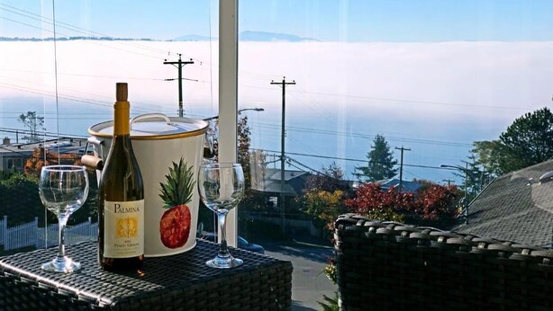 A table with a wine bottle and glasses, overlooking a scenic view of mountains and a body of water. - Star of the sea Guest house, Sea Forever King size bed with ocean view balcony! (White Rock)