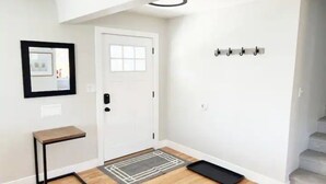 A clean, modern hallway with a white door, a small table, and a coat rack. - 3 Bedroom, Open Layout - Walk to Anschutz Medical! (Aurora)