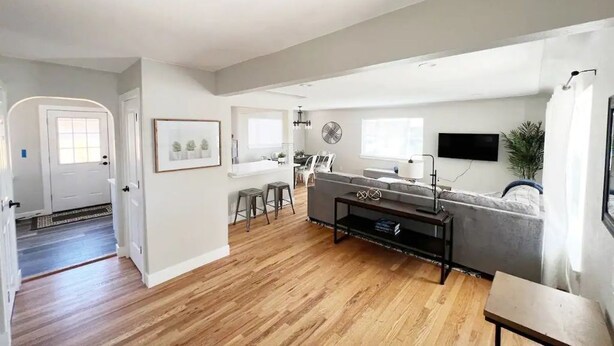 A modern living room with a grey sofa, a coffee table, and a TV. There's a dining area with a table and chairs, and a kitchen in the background. - 3 Bedroom, Open Layout - Walk to Anschutz Medical! (Aurora)