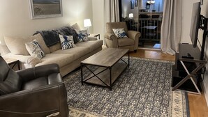 A living room with a sofa, armchair, coffee table, and a TV. There is a patterned rug on the floor and a ceiling fan above. - True Blue Comfy Condo! (Pawleys Island)
