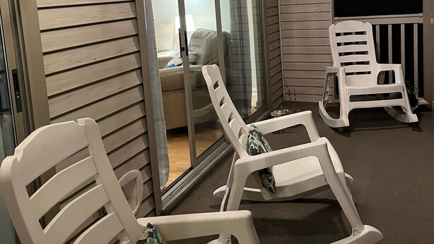 A room with sliding glass doors, white rocking chairs, and a ceiling fan. - True Blue Comfy Condo! (Pawleys Island)