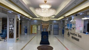 A hotel lobby with a chandelier, reception desk, and a blue emblem on the wall. - Greentree Inn (Suqian)