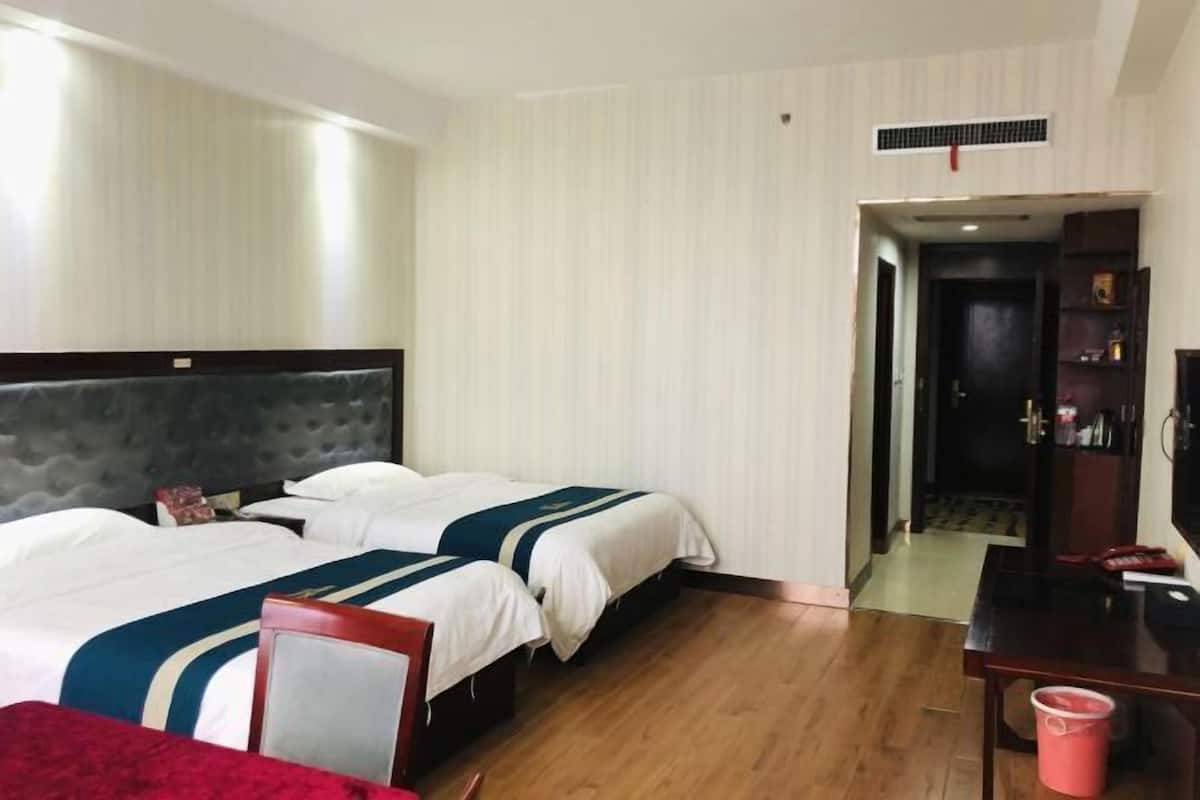 Ein Hotelzimmer mit zwei Betten, einem Schreibtisch, einem Sessel, einem Fernseher und einer Tür zu einem anderen Raum.