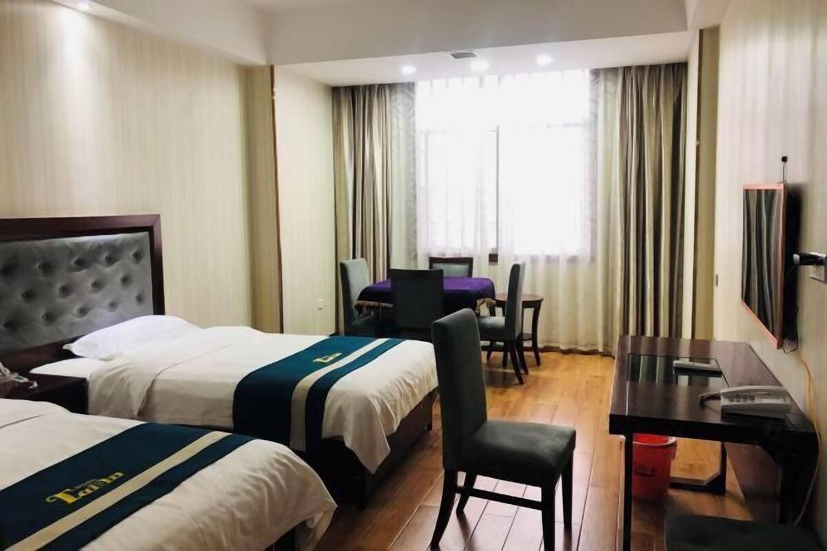 Ein Hotelzimmer mit zwei Betten, einem Schreibtisch, einem Sessel, einem Fernseher und einem Fenster mit Vorhängen.