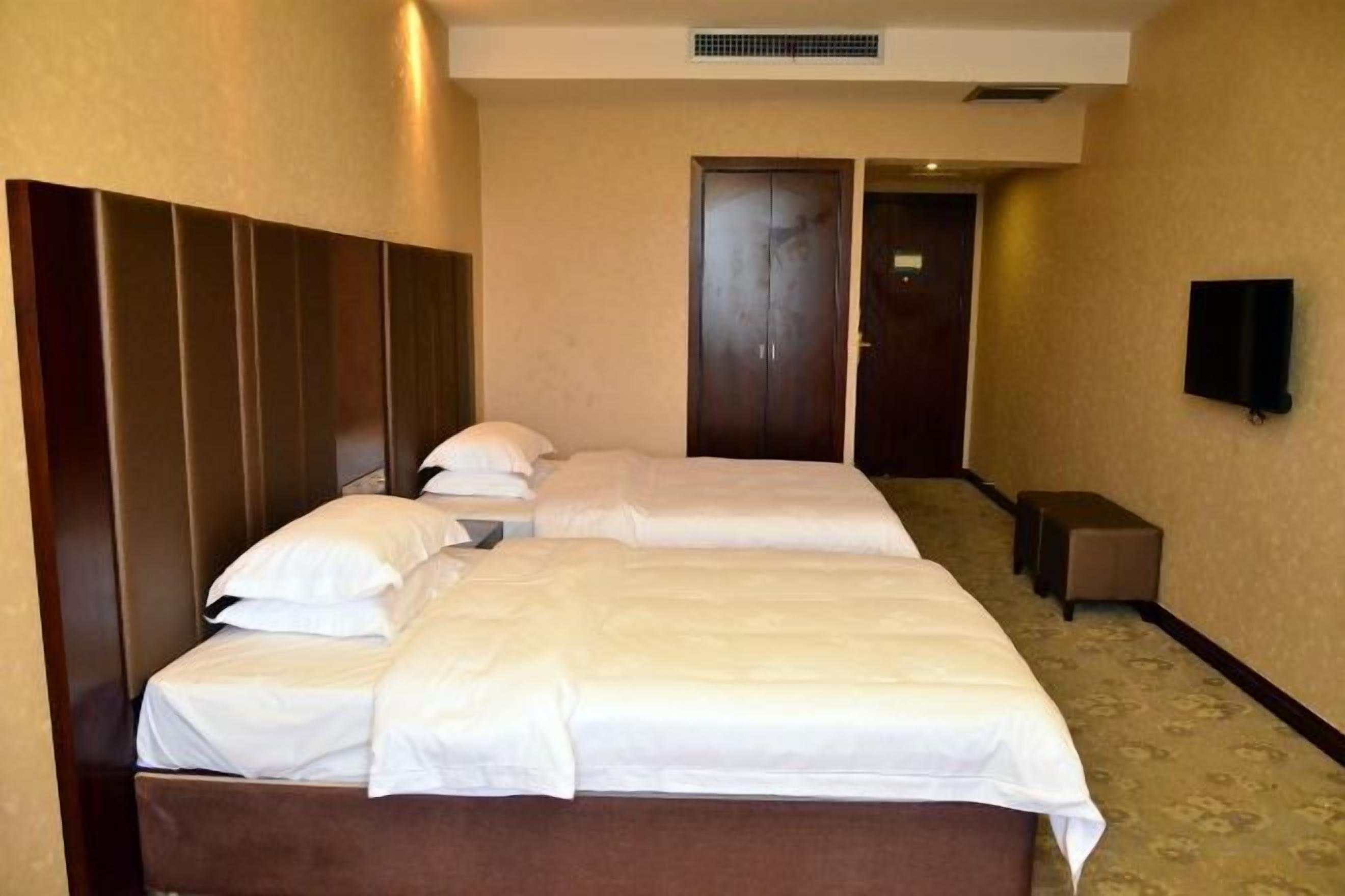 Ein Hotelzimmer mit zwei Betten, einem Kleiderschrank, einem Fernseher und einem kleinen Tisch.