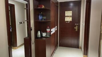 A hallway with a wooden door, a shelf with various items, and a tiled floor.