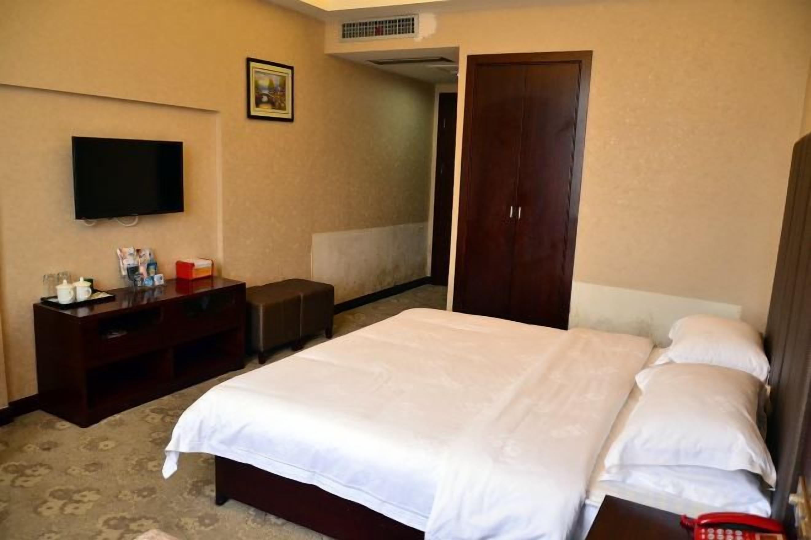 Ein Hotelzimmer mit Bett, Fernseher, Schreibtisch und Kleiderschrank.