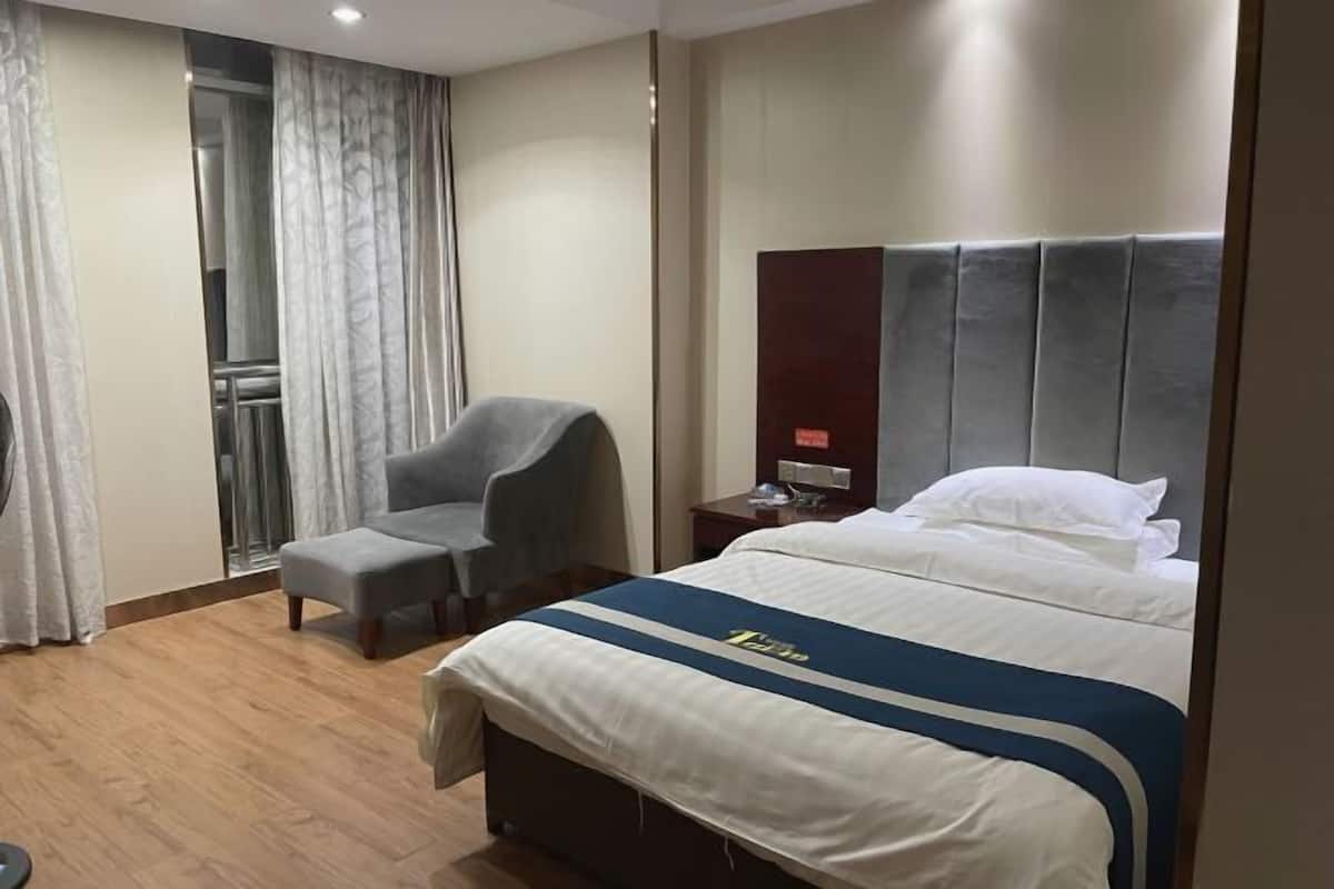 Ein Hotelzimmer mit Bett, Stuhl, Nachttisch und einem Fenster mit Vorhängen.