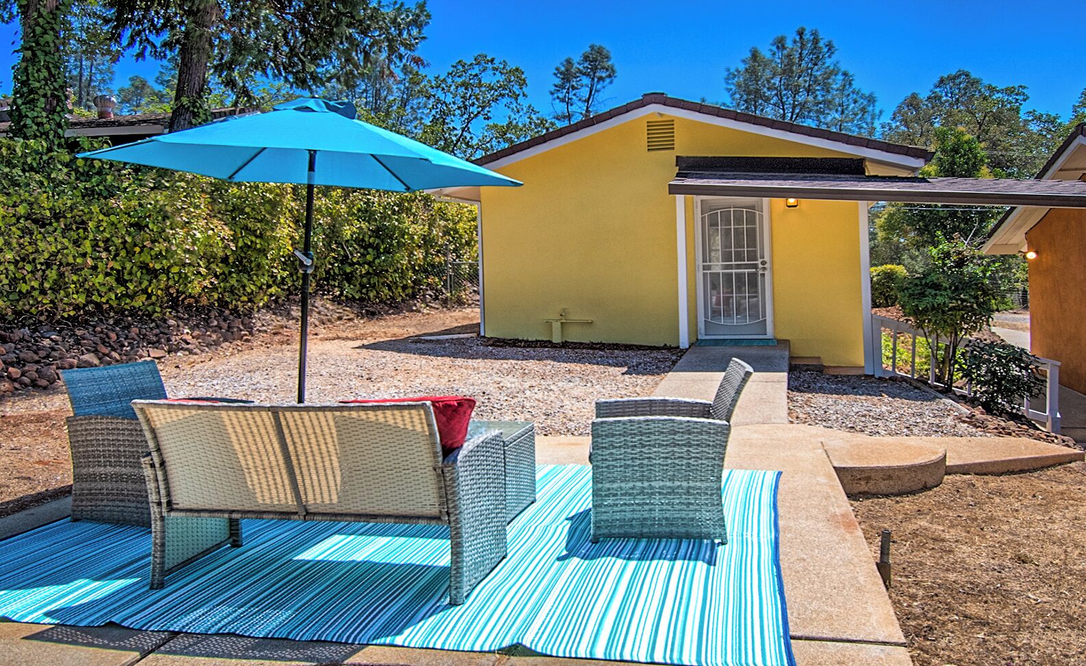 A yellow house with a covered patio area featuring wicker furniture and a blue-striped mat.