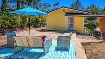 A yellow house with a covered patio area featuring wicker furniture and a blue-striped mat.