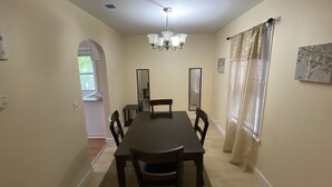 Ein Esszimmer mit einem dunklen Holztisch und Stühlen, einer Kristallleuchtre und einem mit Vorhängen drapierten Fenster.