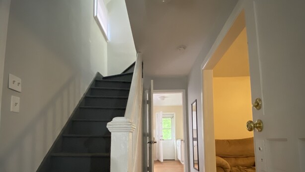 Eine Treppe führt zu einer zweiten Etage, ein Flur mit einer Tür zu einem Wohnzimmer und ein Fenster mit Jalousien.