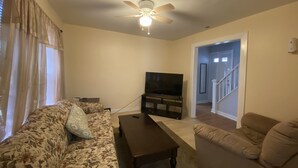 Ein Wohnzimmer mit einer Couch, einem Couchtisch, einem Fernseher und einem Deckenventilator.