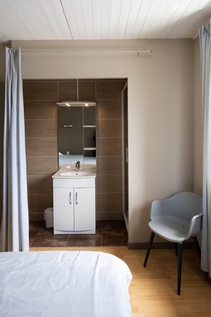 Een moderne slaapkamer met een bed, een witte kast met spiegel, een grijze stoel en een houten vloer.