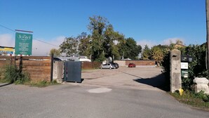 A gated entrance to a property with a signboard, a parking area, and a building in the background. - Le Jostel 2 (Genay)